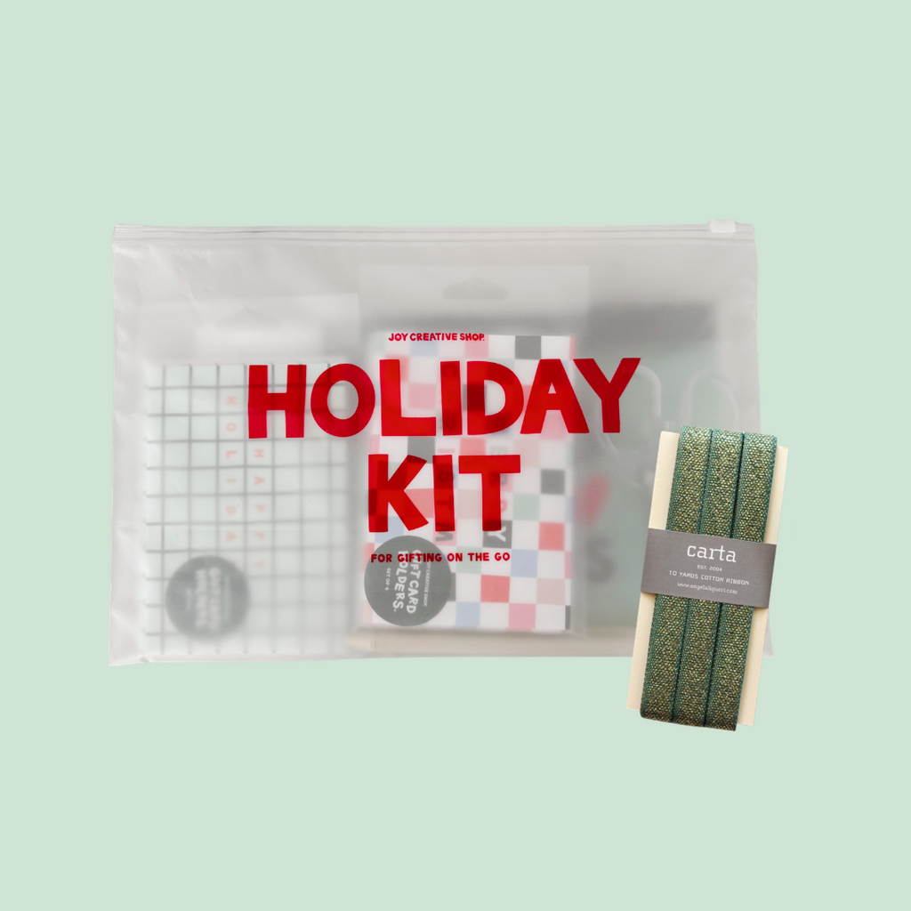 A clear zippered pouch labeled 'HOLIDAY KIT' in large red letters, containing assorted stationery items, shown alongside a packaged green patterned cord or string accessory on a pale mint background.
